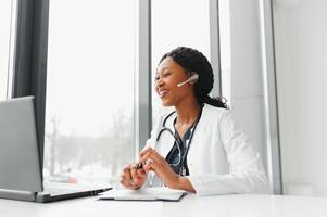 africano americano mujer médico trabajando a su oficina en línea utilizando portátil informacion dispositivo. telemedicina servicios. primario cuidado consultas, psicoterapia, emergencia servicios foto