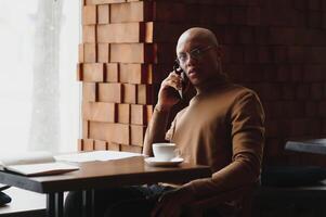 African-Ameican entrepreneur wearing shirt with rolled up sleeves looking through window with thoughtful and serious face expression, feeling nervous before meeting with business partners at cafe. photo