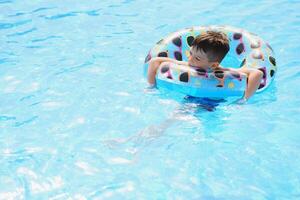 contento chico en nadando piscina. chico es solo, nadando inflable anillo y rodeado por agua salpicaduras mojado adolescente es disfrutando verano fin de semana en diversión agua parque. bandera con Copiar espacio foto