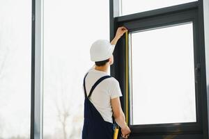 obrero en mono instalando o ajustando el plastico ventanas en el vivo habitación a hogar foto