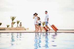 young family with suitcases walking to hotel building with beautiful swimming pool. traveling and relaxing time concept. photo