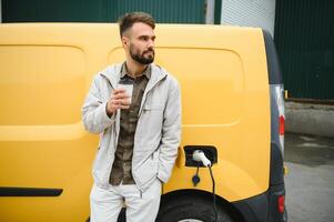 Handsome man drinking coffee while charging electric car photo