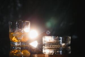 A glass of whiskey or Bourbon with ice cubes and a cigar on a black slate with smoke photo