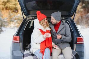 sonriente juntos. bonito Pareja tener fin de semana a campo a invierno tiempo. sentado en el posterior parte de moderno coche. foto