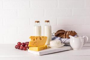A bottle with milk, a with fresh cottage cheese and cheese on a wooden board and a white background. Traditional dairy products for Shavuot photo