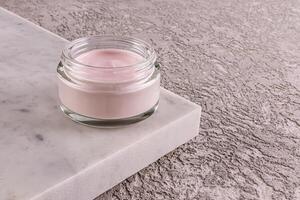 Fashionable cosmetic product in glass jar, delicate pink cream for young skin care on marble podium and gray cement background photo