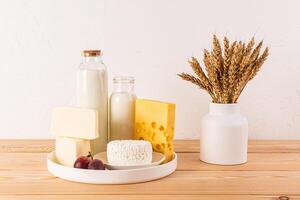 Fresh dairy products, cheese, bottle milk on a white dish and a wooden table with a vase with ears of corn. Concept of the Jewish holiday of Shavuot. photo