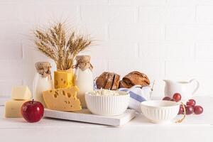 A different cheese, bread, cottage cheese, sour cream, milk in bottles on a white wooden countertop. Concept of the Jewish holiday of Shavuot. photo