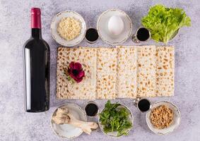 Flat lay of traditional products for the Jewish Passover holiday. Wine, matzoth bread, parsley, lettuce, egg, bone. Top view. grey marble background photo