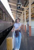 joven mujer con maleta murga a el metro estación mientras el tren llega, turismo y viaje en el verano. vacaciones para el alumno. trabajo y viaje foto