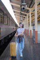 joven mujer con maleta murga a el metro estación mientras el tren llega, turismo y viaje en el verano. vacaciones para el alumno. trabajo y viaje foto