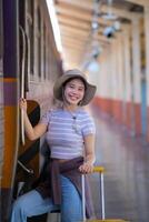 joven mujer con maleta murga a el metro estación mientras el tren llega, turismo y viaje en el verano. vacaciones para el alumno. trabajo y viaje foto