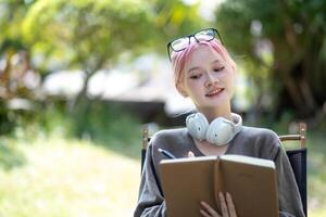 Young Happy Asian artist woman drawing book and wearing headphone, the artist paints in the garden photo