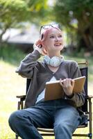 Young Happy Asian artist woman drawing book and wearing headphone, the artist paints in the garden photo