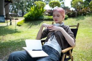 Young Happy Asian artist woman drawing book and wearing headphone, the artist paints in the garden photo