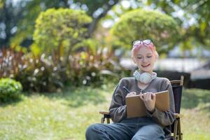 Young Happy Asian artist woman drawing book and wearing headphone, the artist paints in the garden photo