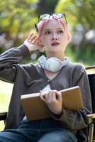 Young Happy Asian artist woman drawing book and wearing headphone, the artist paints in the garden photo