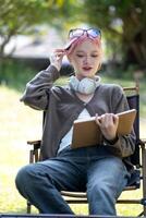 Young Happy Asian artist woman drawing book and wearing headphone, the artist paints in the garden photo