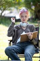 Young Happy Asian artist woman drawing book and wearing headphone, the artist paints in the garden photo