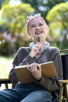 Young Happy Asian artist woman drawing book and wearing headphone, the artist paints in the garden photo