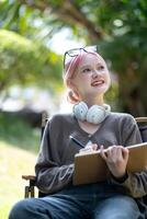 Young Happy Asian artist woman drawing book and wearing headphone, the artist paints in the garden photo