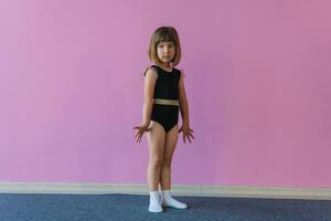 Very cute beautiful girl with blond hair in a black glamorous leotard stands on pink background photo