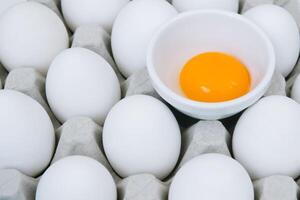 White raw chicken eggs and alone broken brown egg in a tray top view photo