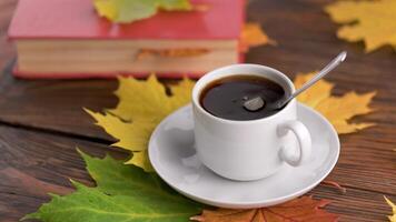 coffe cup on wooden table with book and colorful autumnal maple leaves with spinning coffee bubbles video