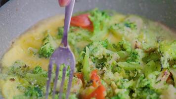 hand with fork picks frying vegetables with egg yolk close-up video