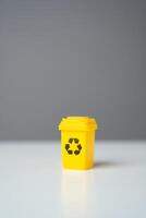 Yellow recycling bin on gray background. Selling recycled material or getting grants for green projects. Circular economy. Conserve natural resources, reduce waste, create jobs in recycling industry. photo