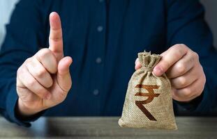 A man warns with his finger offering a indian rupee money bag. Funding and grants. Banks and finance. Bad credit history. Strict conditions. Loan for a specific purpose. Terms of borrowing money. photo