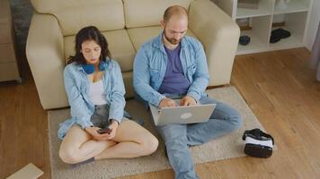 Young couple relaxing on carpet using laptop and smartphone video
