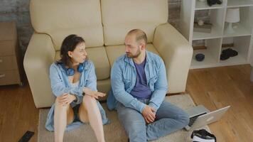 Top view of couple having a conversation sitting near sofa on carpet. video