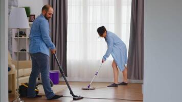 Husband and wife cleaning their house together using vacuum and mop. video
