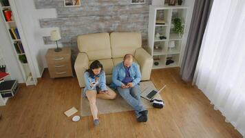 Top view of caucasian couple in denim browsing on smartphone on the floor of their apartment video