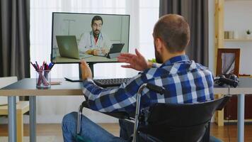 Young guy in wheelchair talking with his doctor about the process of rehabilitation on video call.