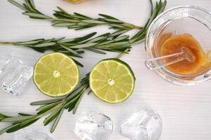 Lime, honey, rosemary and ice cube on a white table. Ingredients for healthy lemnade. photo