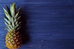 Pineapple on the dark blue wooden table. Summer flat lay. Background with place for text. photo