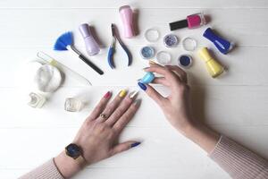 A woman painting her nails. Tools for manicure on a white wooden table. photo