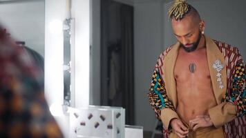 ein Mann mit ein Mohawk und ein bunt Jacke ist suchen im das Spiegel video