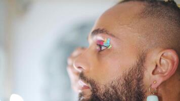 a man with a beard and a gold hair piece applying make up in front of the mirror video