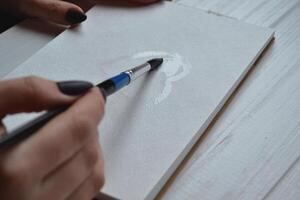 Woman paints in a sketchbook. Tools for painting on the white wooden desk. Painter work. photo