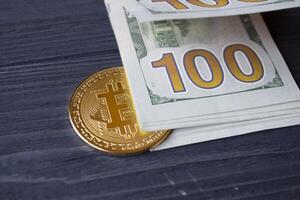 Golden bitcoin and dollars in male hand on a dark blue wooden background. Gold coin of cryptocurrency. photo