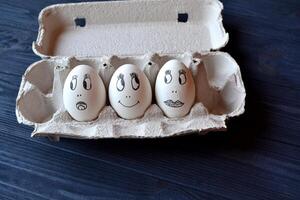 Eggs with a faces in a container box on the wooden table. Creative easter background. Happy easter day. photo