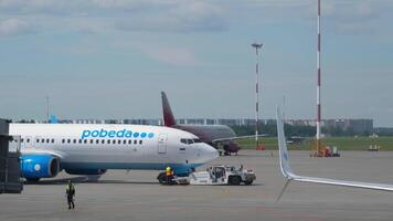 SAINT PETERSBURG, RUSSIA - JULY 26, 2022 - Boeing 737 of Pobeda with tug at Pulkovo airport, St. Petersburg. Tractor pulling plane on the taxiway video