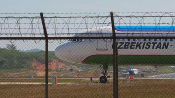 PHUKET, THAILAND - FEBRUARY 10, 2023 - Passenger plane Airbus A321, UK32103 Uzbekistan Airways taxiing on the runway at Phuket airport, side view through the fence video