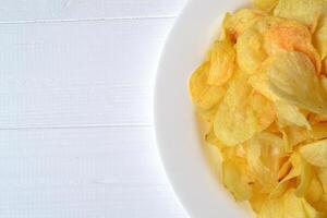 Chips in the white plate on the white wooden table. Fast food. Fried potatoes. photo