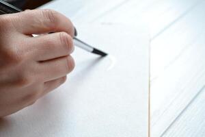 Woman paints in a sketchbook. Tools for painting on the white wooden desk. Painter work. photo