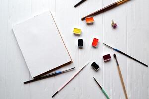 Tools for painting on the white wooden desk. Brushes, paper and paints on the table. Painter's workplace. photo