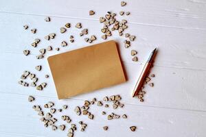 vacío papel y bolígrafo con decorativo de madera corazones en el blanco escritorio. foto